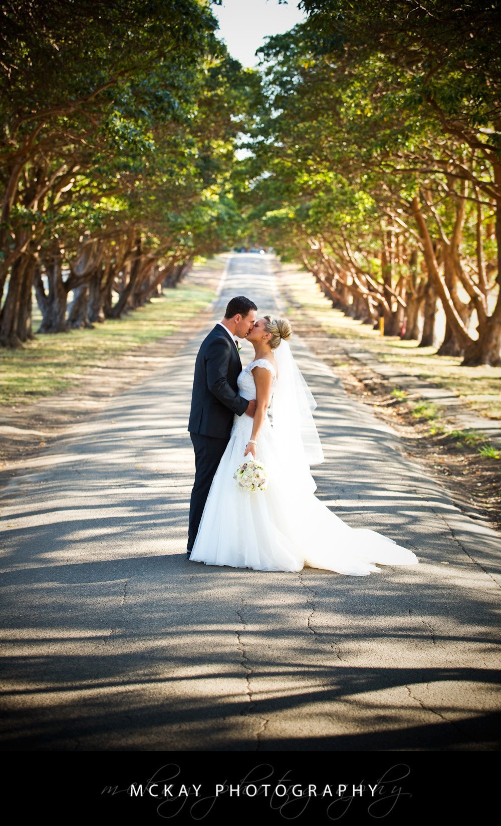 bride and groom kissing driveway trees